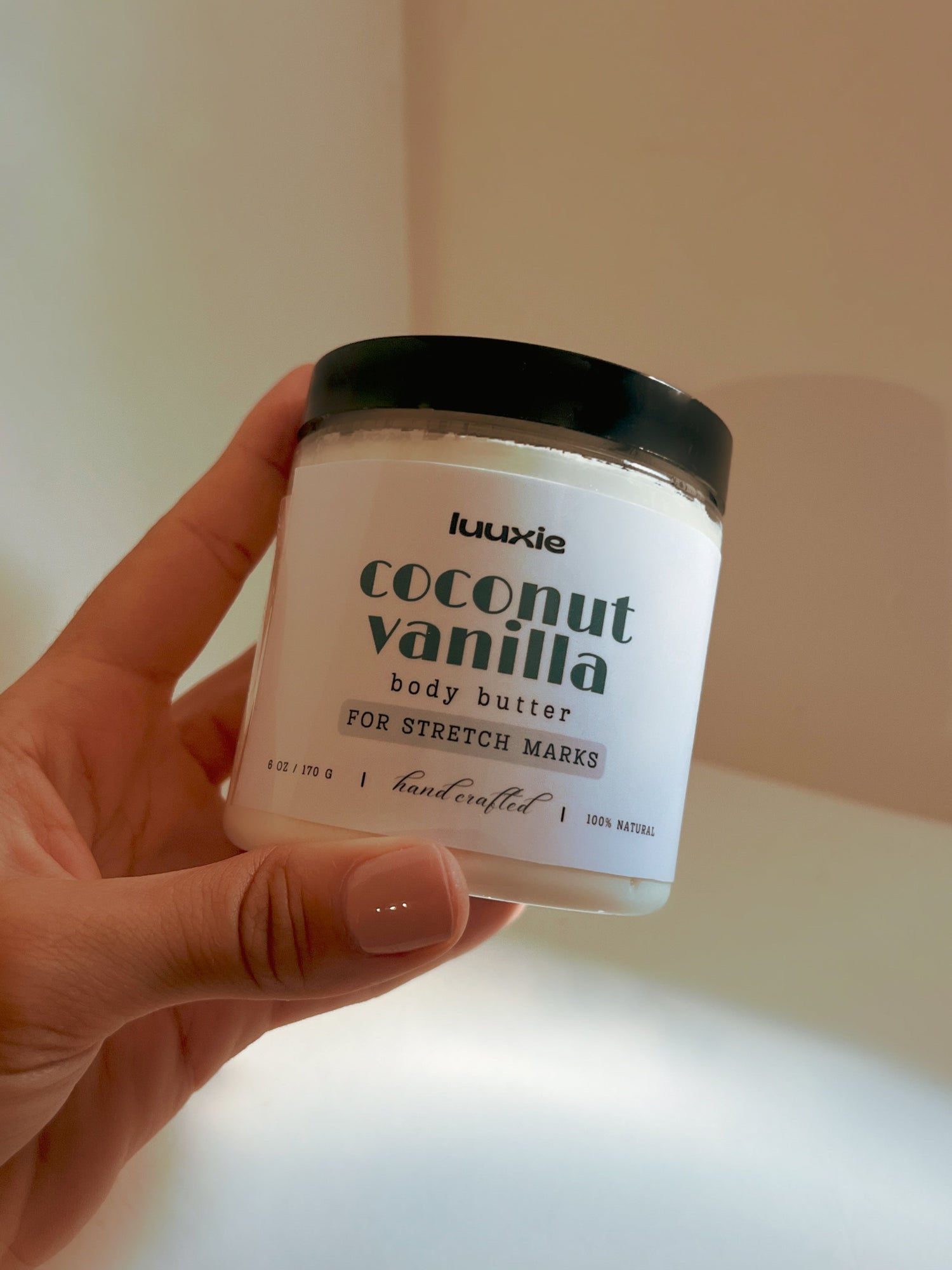 Hand holding a jar of coconut vanilla body butter against a neutral background